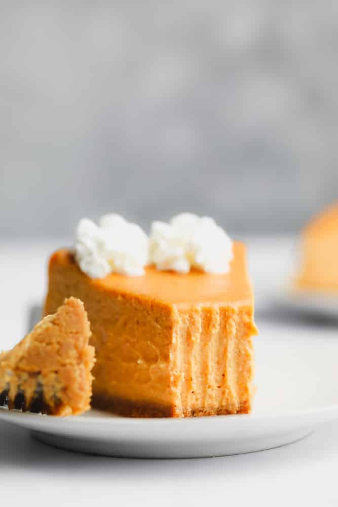 a slice of pumpkin cheesecake topped with whipped cream and a bite removed.