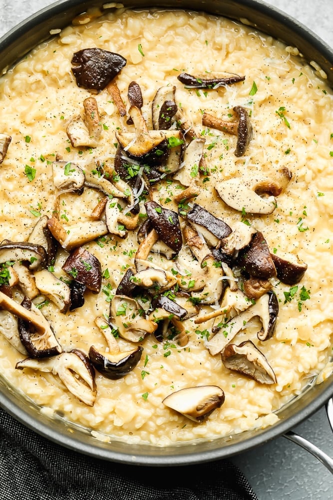 creamy yellow risotto topped with cooked mushrooms in a large black pan.
