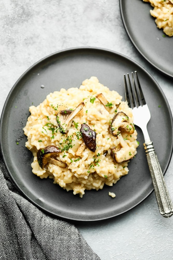 a scoop of creamy risotto topped with cooked mushrooms on a grey plate with a fork.