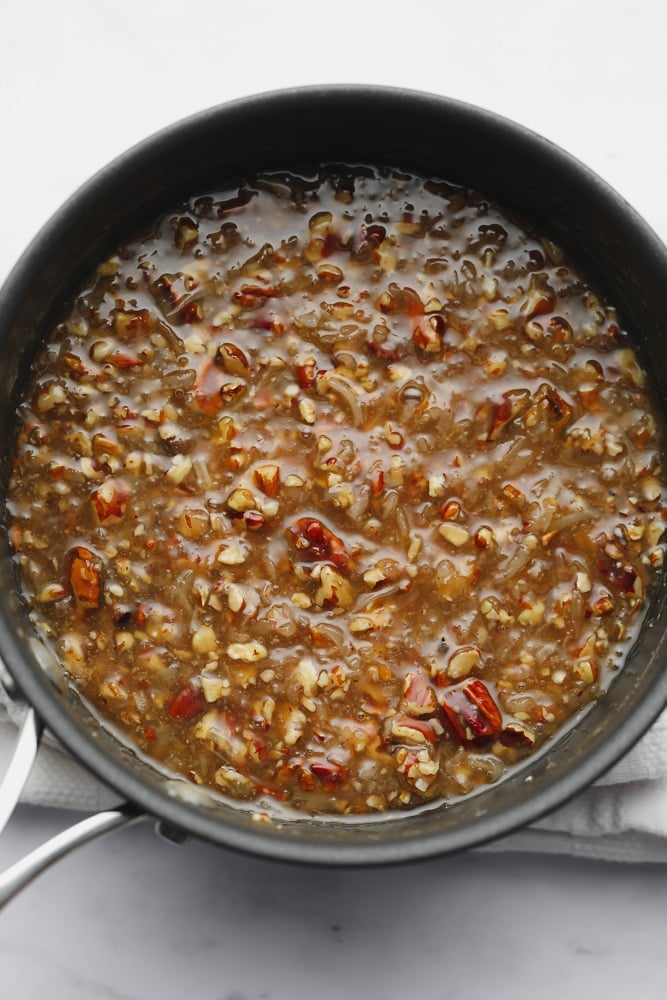 a brown caramel liquid with pecans in a black pot.