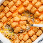 metal spoon scooping some baked tater tot casserole out of a white casserole dish.