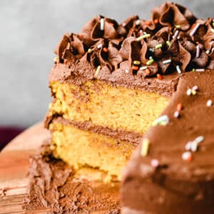 yellow cake with chocolate frosting with slices missing on a wood board.
