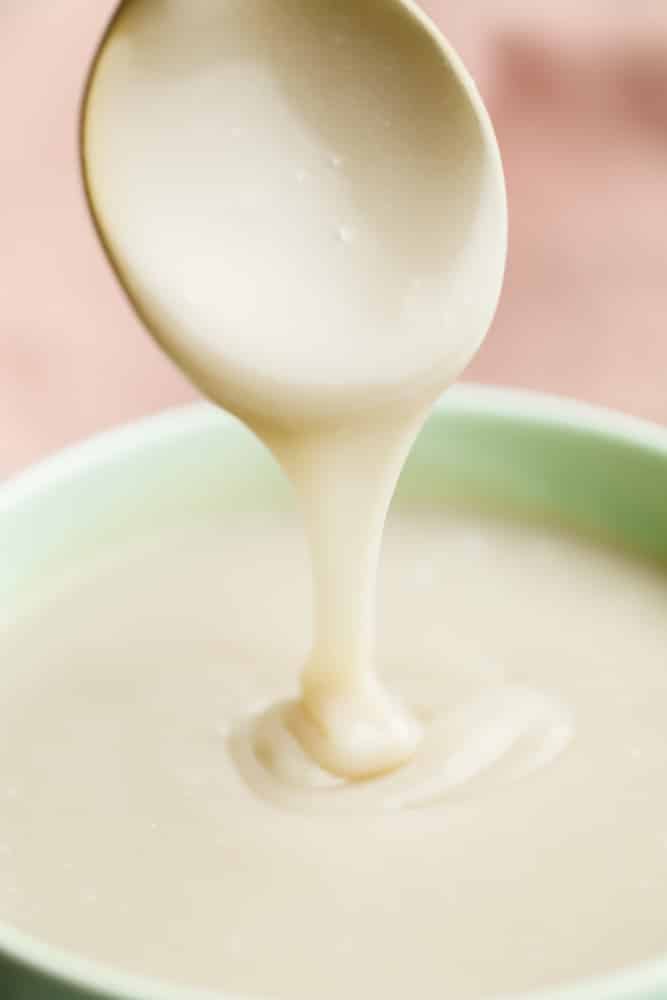 A spoon drizzling a creamy white liquid into a green bowl.