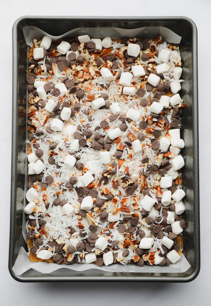a metal baking pan filled with chocolate chips, mini marshmallows, coconut, and nuts.