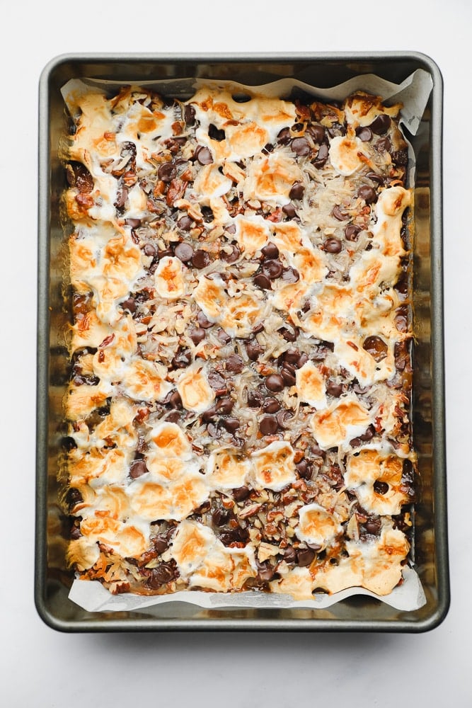 baked cookie bars topped with toasted marshmallows and chocolate in a metal baking pan.