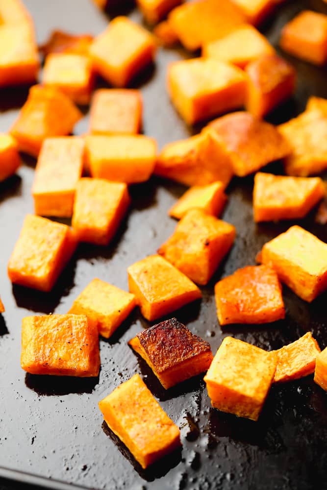 close up on roasted butternut squash cubes on a black baking sheet.