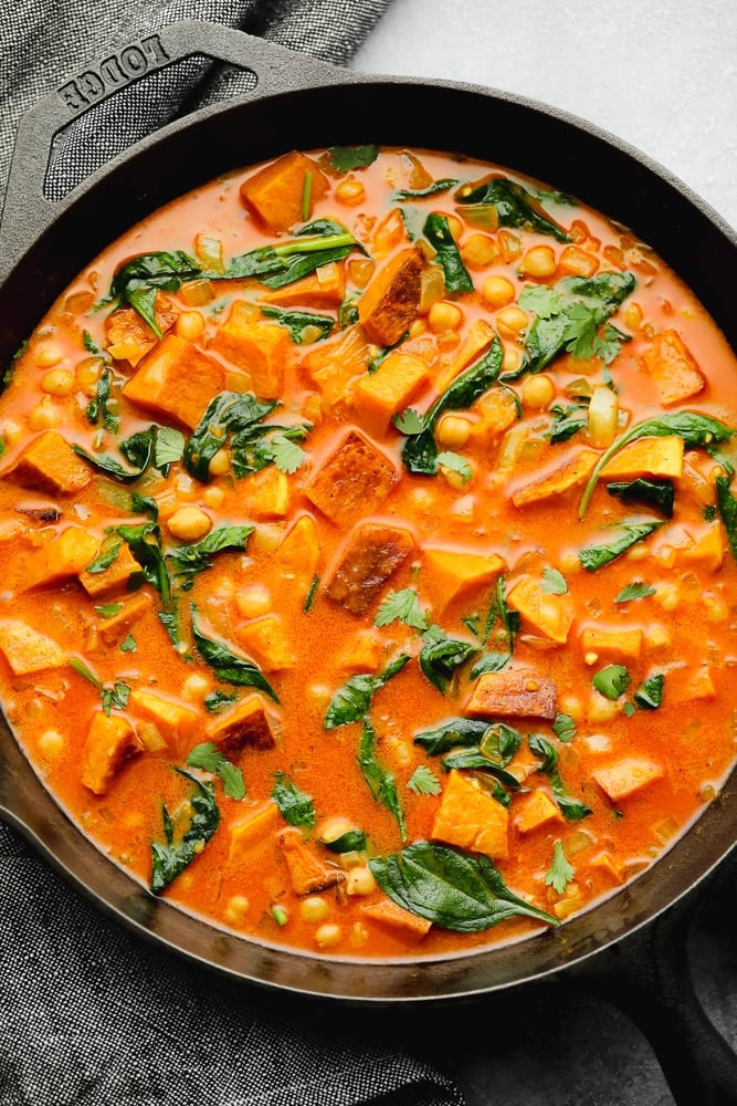 wilted spinach, cubed butternut squash, and chickpeas in an orange liquid in a black skillet.