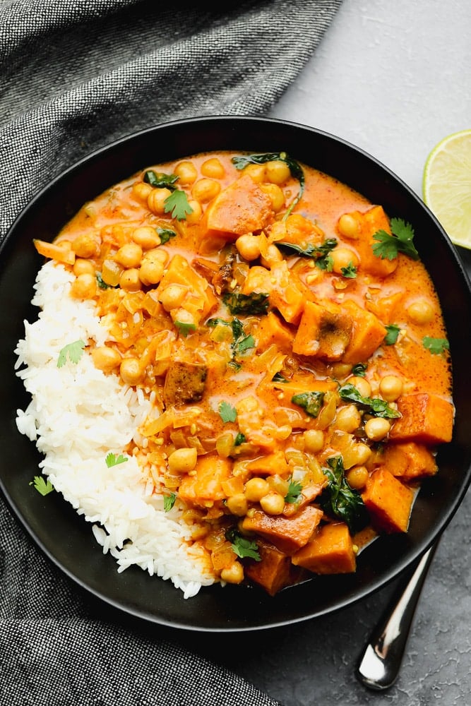 a black bowl filled with an orange butternut squash curry and white rice.