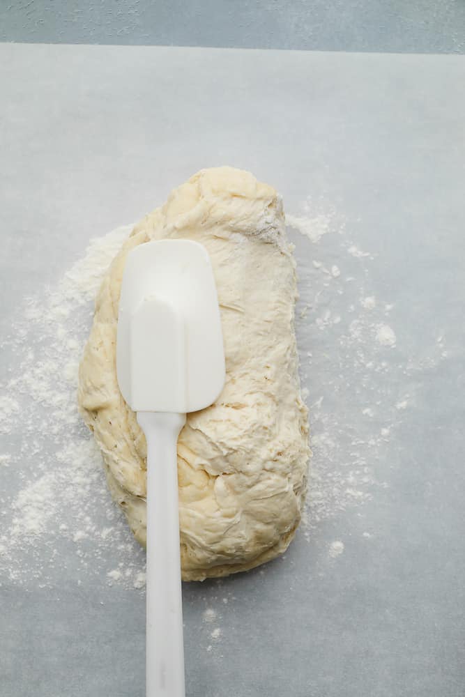 white spatula on top of a raw ball of bread dough.