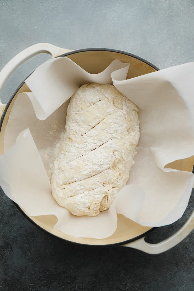 raw bread dough in a white dutch oven and surrounded by parchment paper.