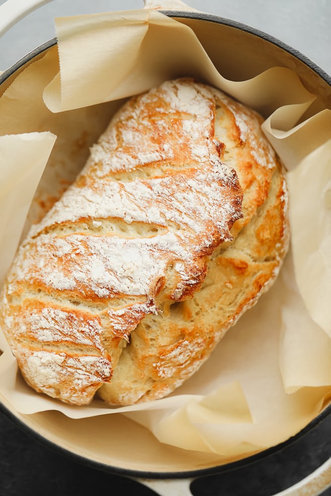 baked golden brown bread in a dutch oven surrounded by parchment paper.