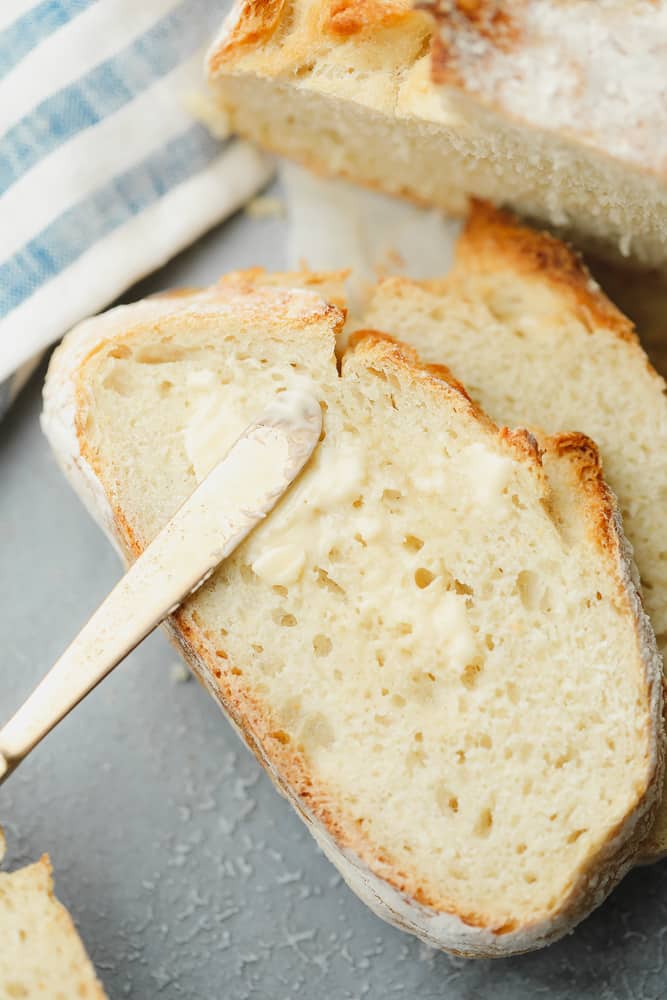 knife spreading butter onto a piece of baked bread.