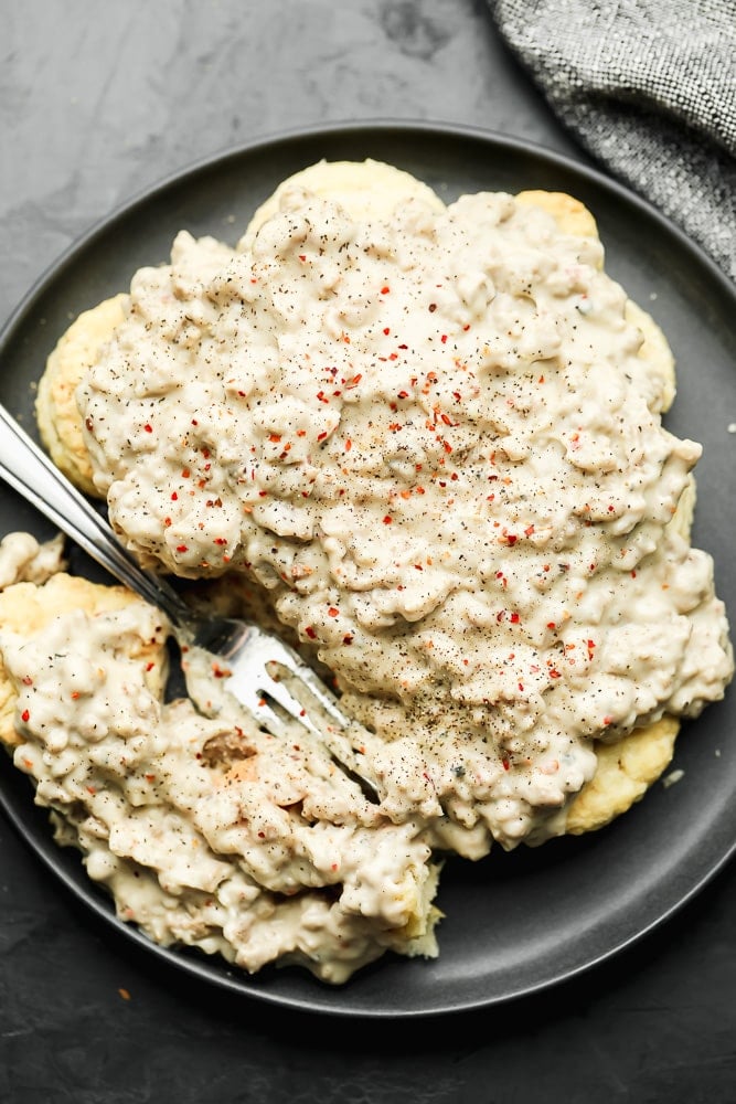 black plate with vegan biscuits and sausage gravy, with a fork in it