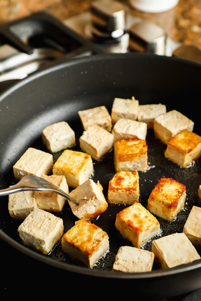 showing flipping tofu over in a pan with a fork