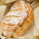 baked golden brown bread in a dutch oven surrounded by parchment paper.