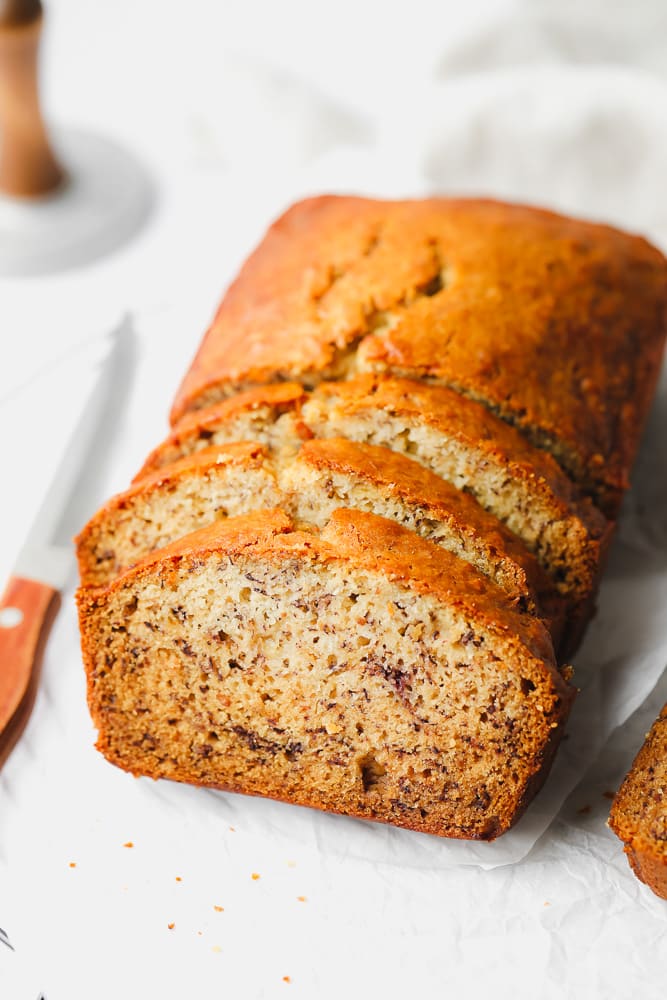 3 slices of vegan banana bread on parchment paper with the rest of the loaf in background