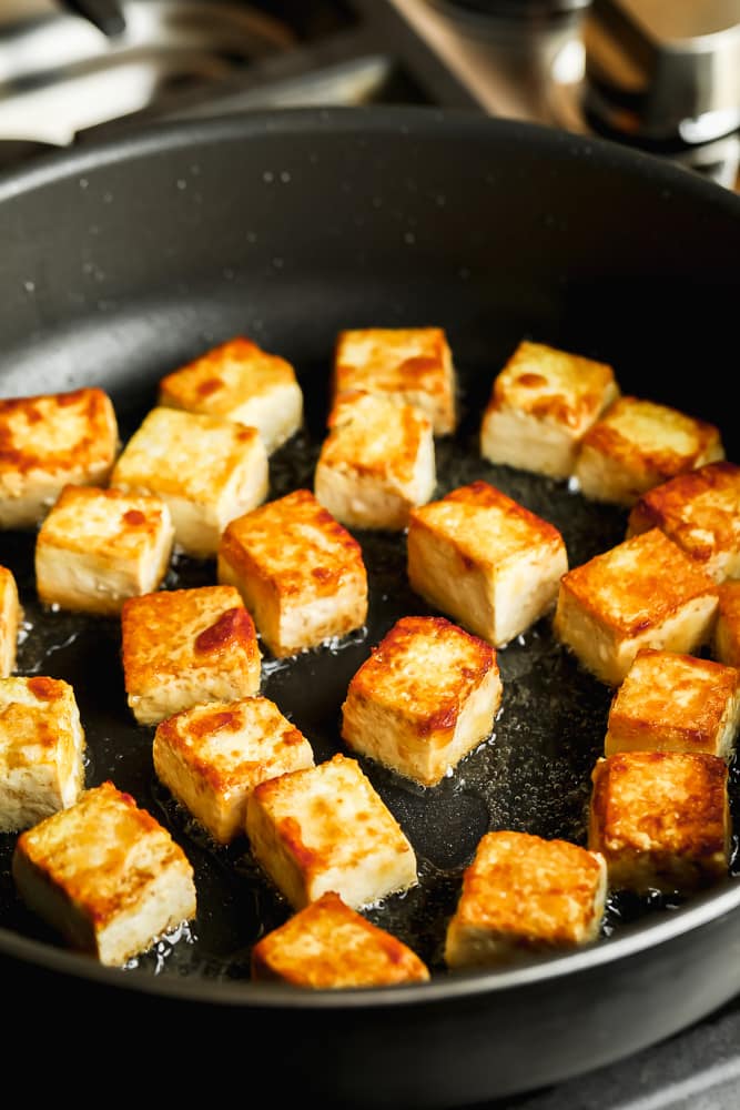 close up on tofu cubes frying in a large black skillet.