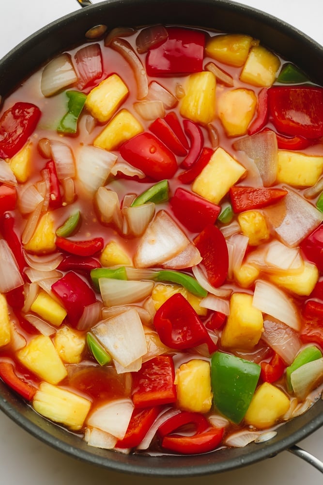 chopped onions, pineapple chunks, red and green bell peppers, and red sauce in a large black skillet.