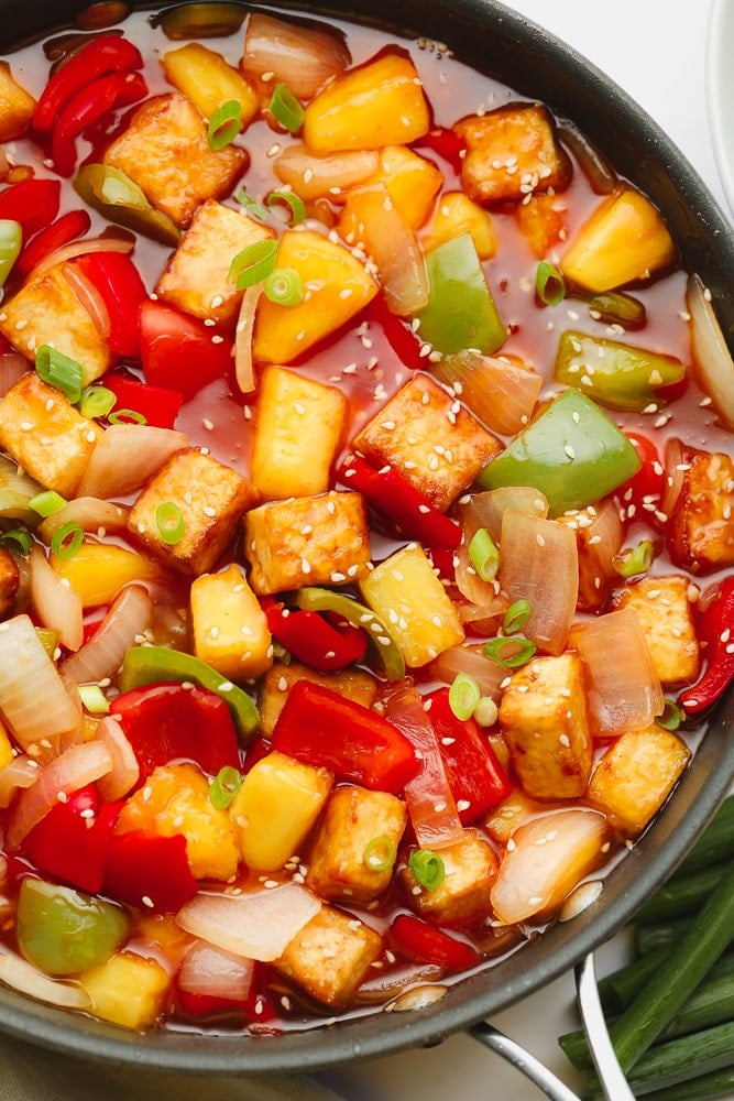 black skillet filled with red sauce, cooked peppers, onions, pinapple, and tofu cubes.