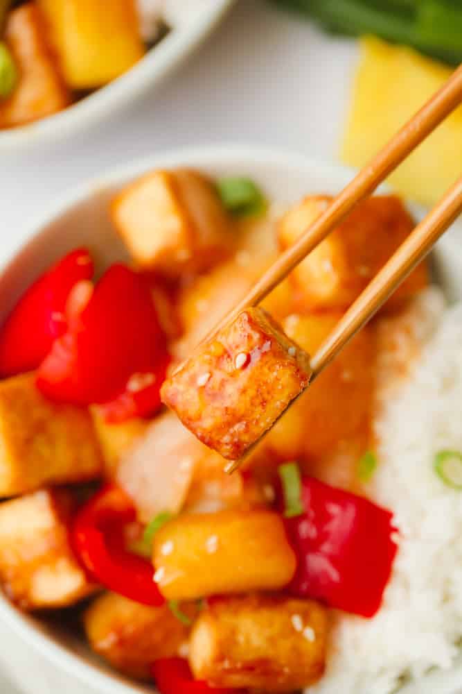 close up on wood chopsticks holding a fried tofu cube.