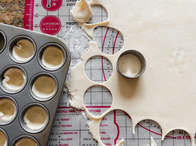 pie crust dough being rolled out onto a pastry mat and cut into small circles