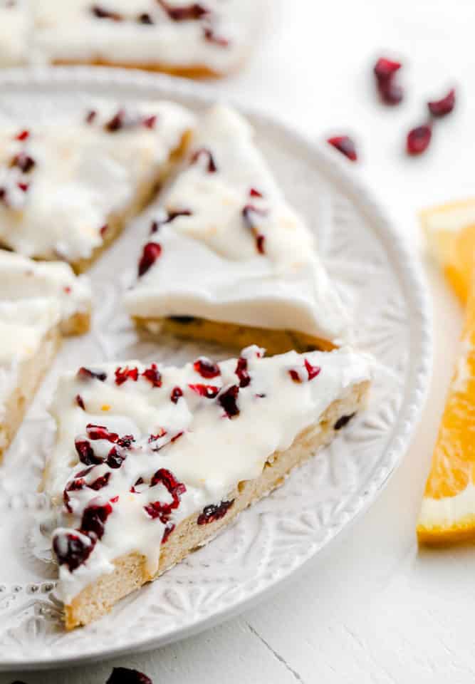 close up on vegan cranberry bliss bars cut into triangles on a white plate.