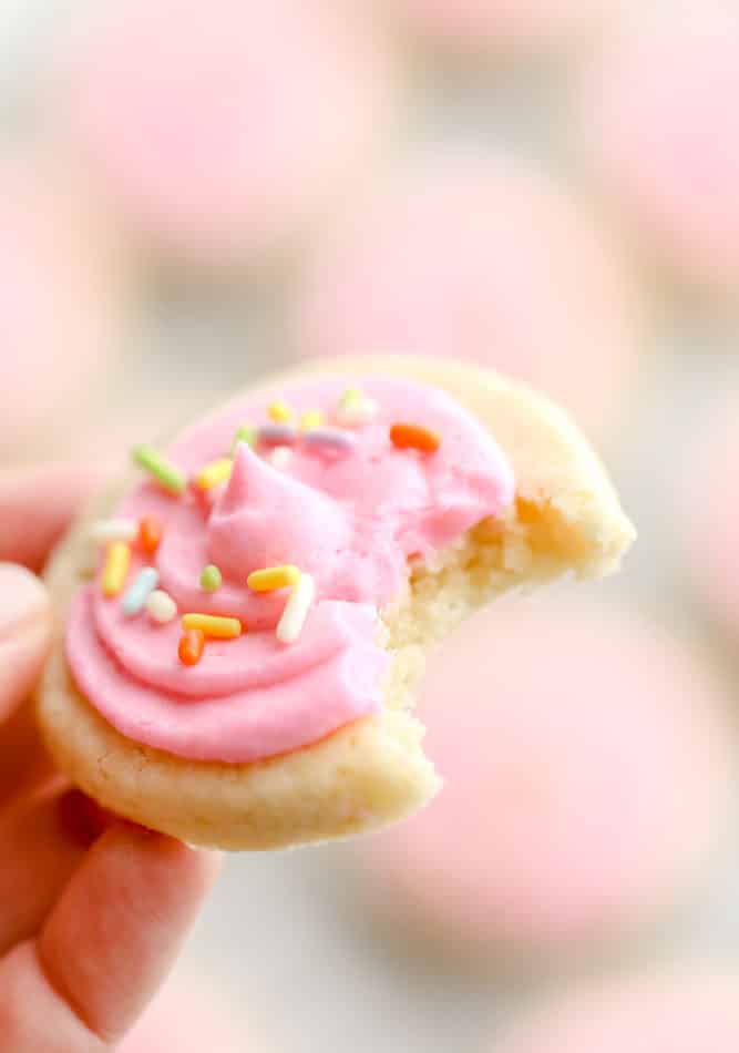 hand holding up a cookie with a bite taken out with pink frosting and sprinkles
