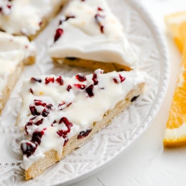 close up on vegan cranberry bliss bars cut into triangles on a white plate.