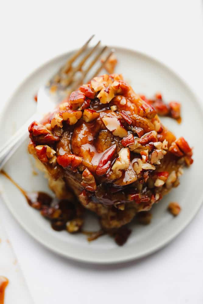 cinnamon roll with pecans on a plate with fork and white background