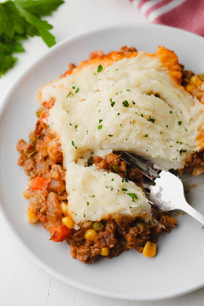 close up of a fork taking a bite out of a meaty pie with potatoes on top