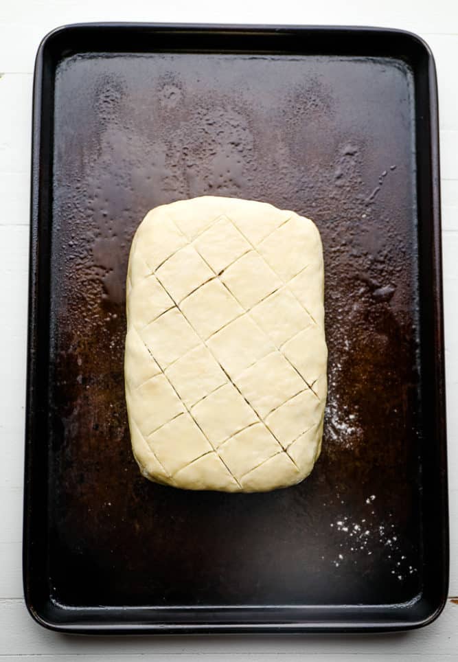 an uncooked puff pastry-wrapped loaf on a metal baking sheet.