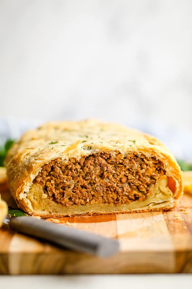 a baked vegan beef wellington cut in half on a wood board.