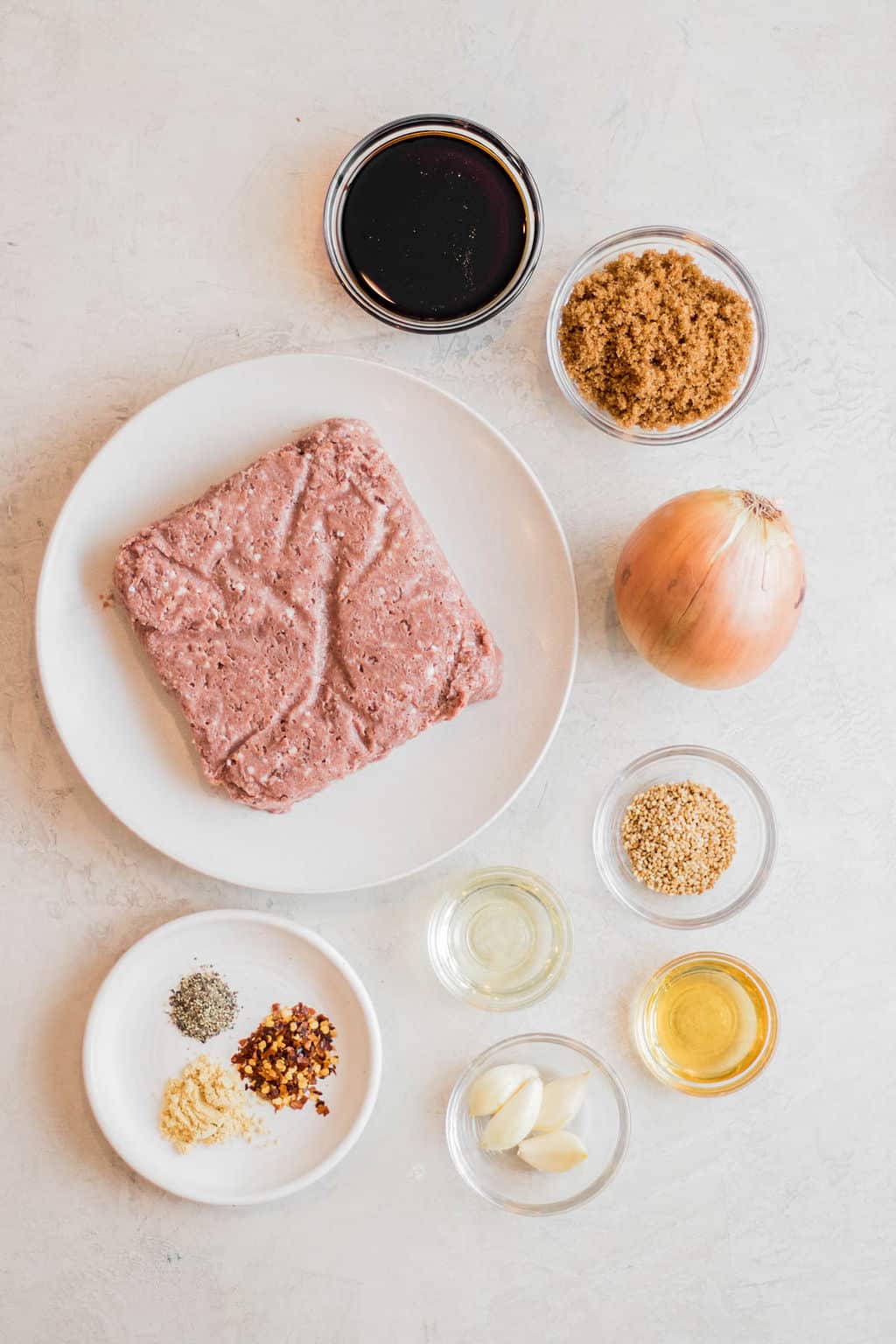 raw vegan beef on a white plate next to small bowls of sauces, seasonings, onion, and brown sugar.