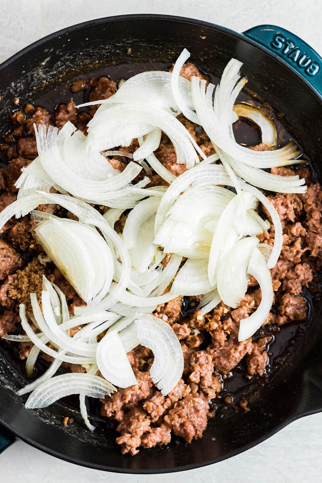raw onions on top of cooked vegan ground beef in a black skillet.