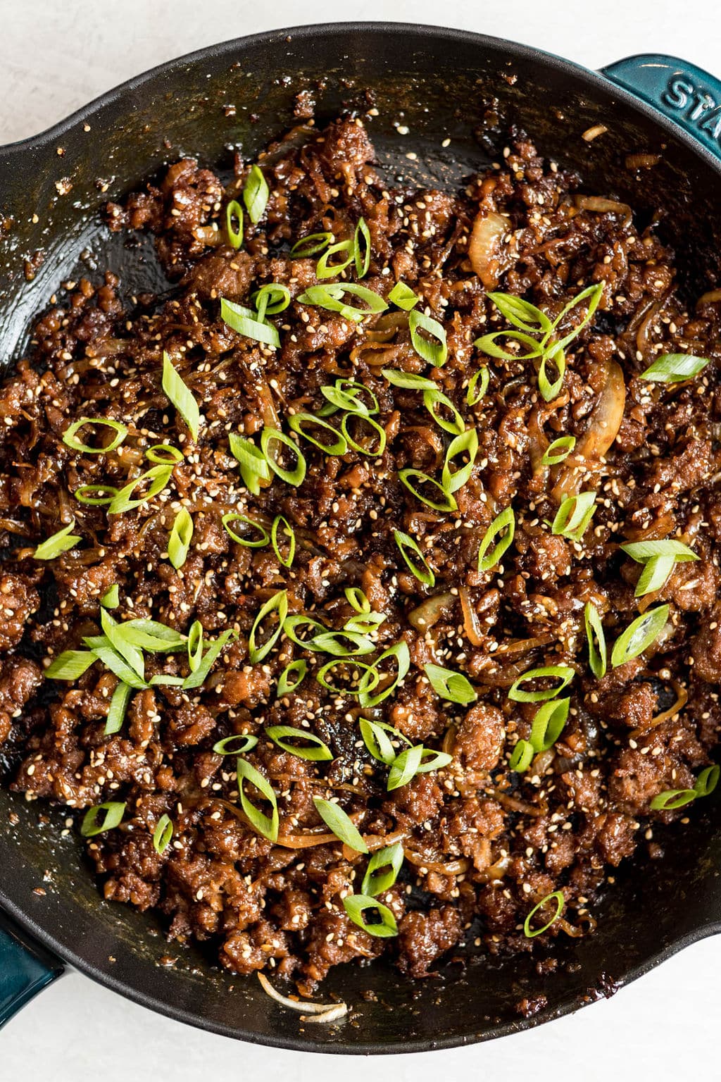 cooked vegan ground beef and onions covered in green onions in a black skillet.