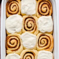 square image of cinnamon rolls, some with frosting, in white dish