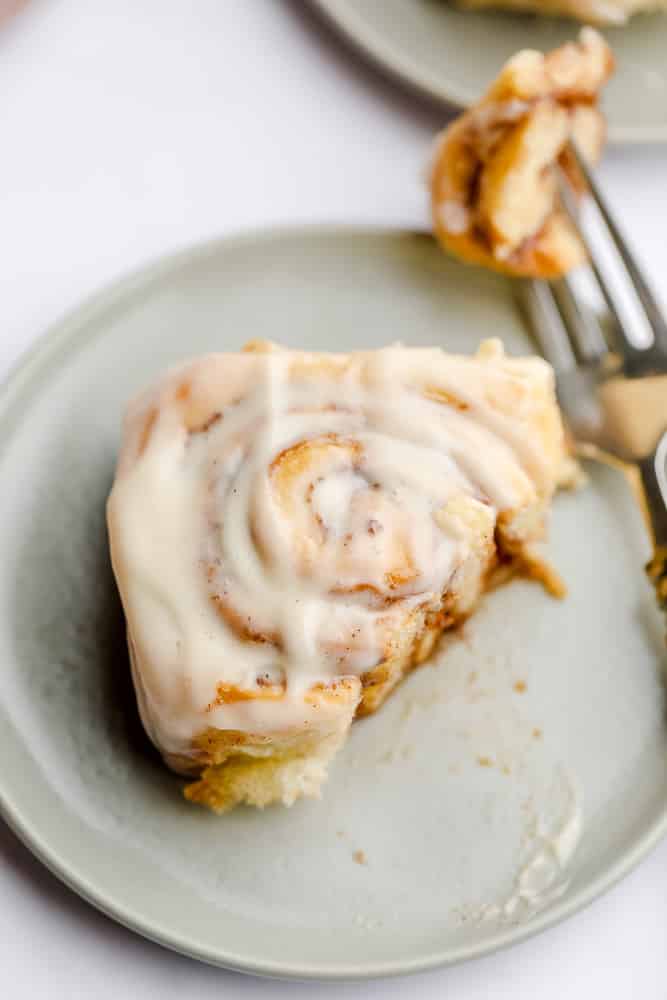 cinnamon roll on a grey plate with fork taking a bite out of it