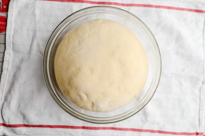 ball of dough on a red striped towel in glass bowl