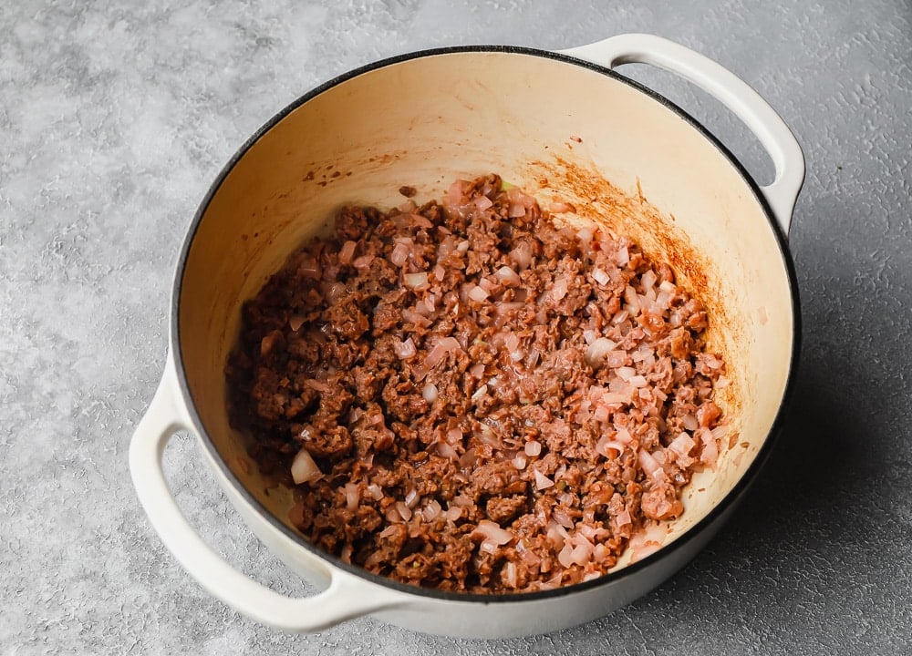 Sauteeing vegan beef and tomatoes in a large white pot.