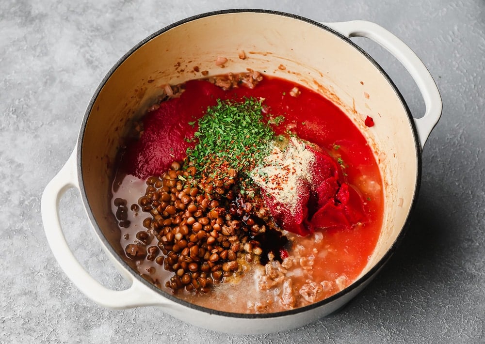 lentils, tomato sauce, green herbs, and spices cooking together in a large white pot.