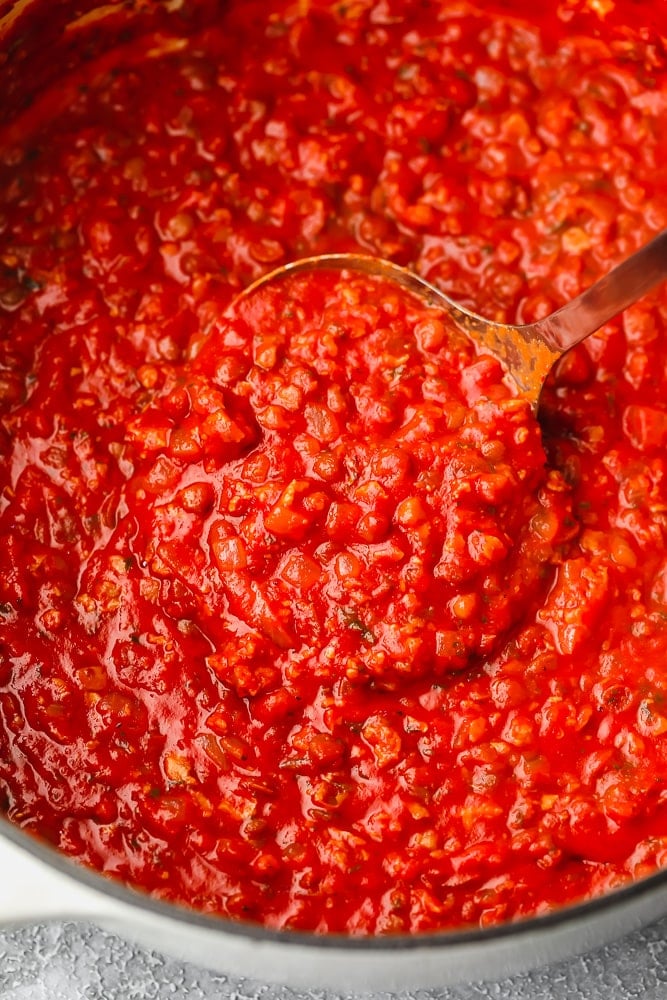 close up on a ladle taking a scoop of red tomato sauce out of a pot.