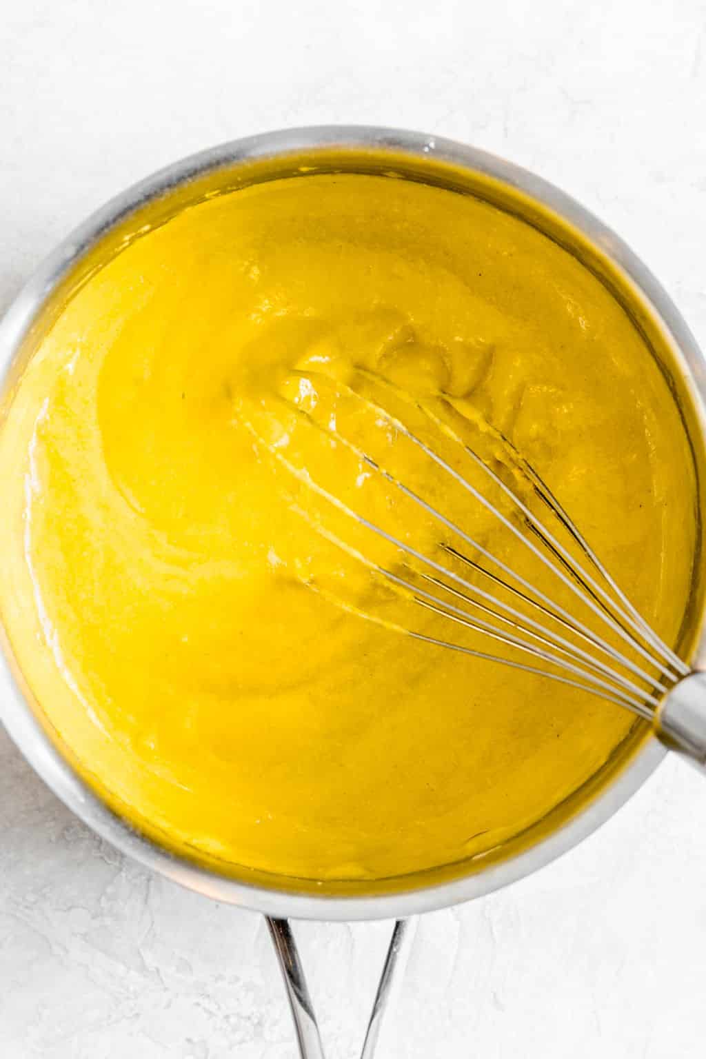 whisking an orange sauce in a metal pot.