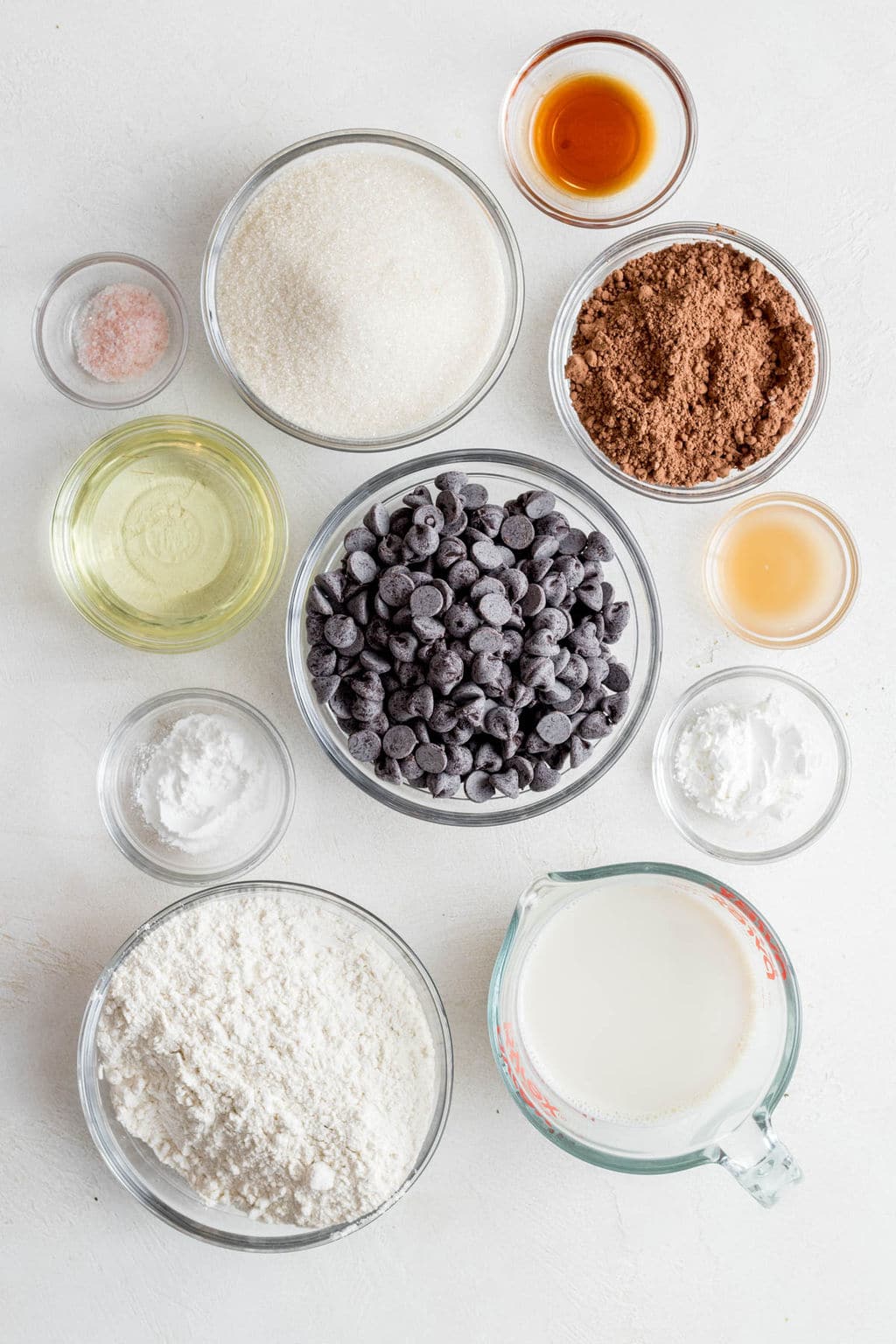 small glass bowls filled with flour, milk, cocoa powder, chocolate chips, and oil.