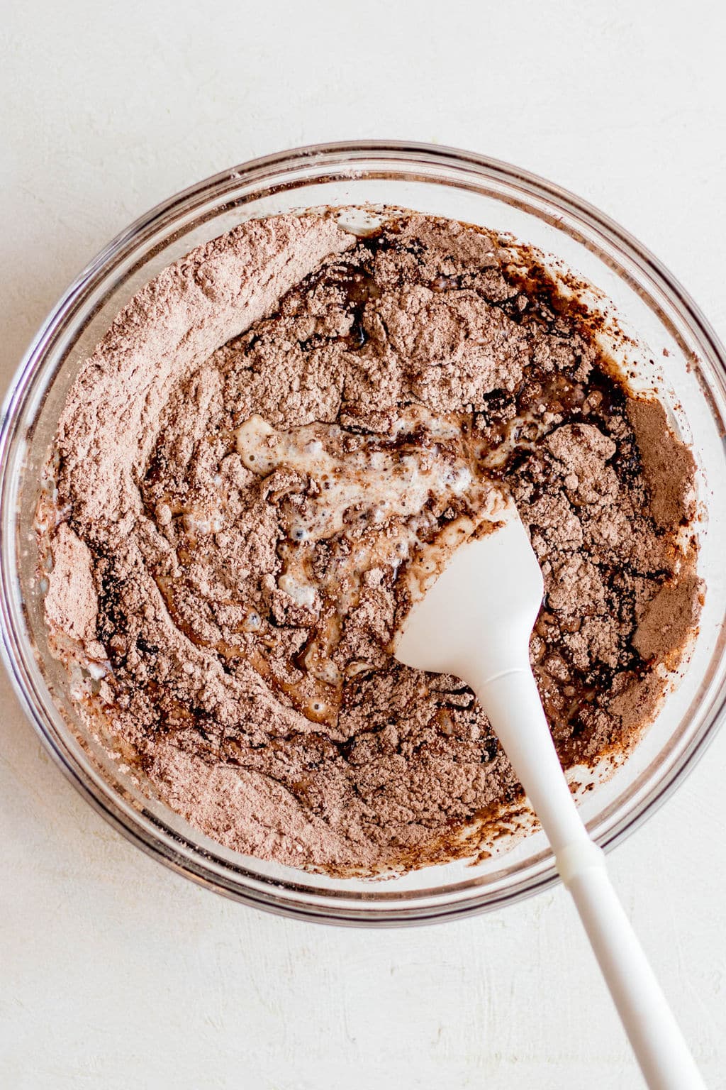 white spatula stirring chocolate muffin batter in a glass bowl.