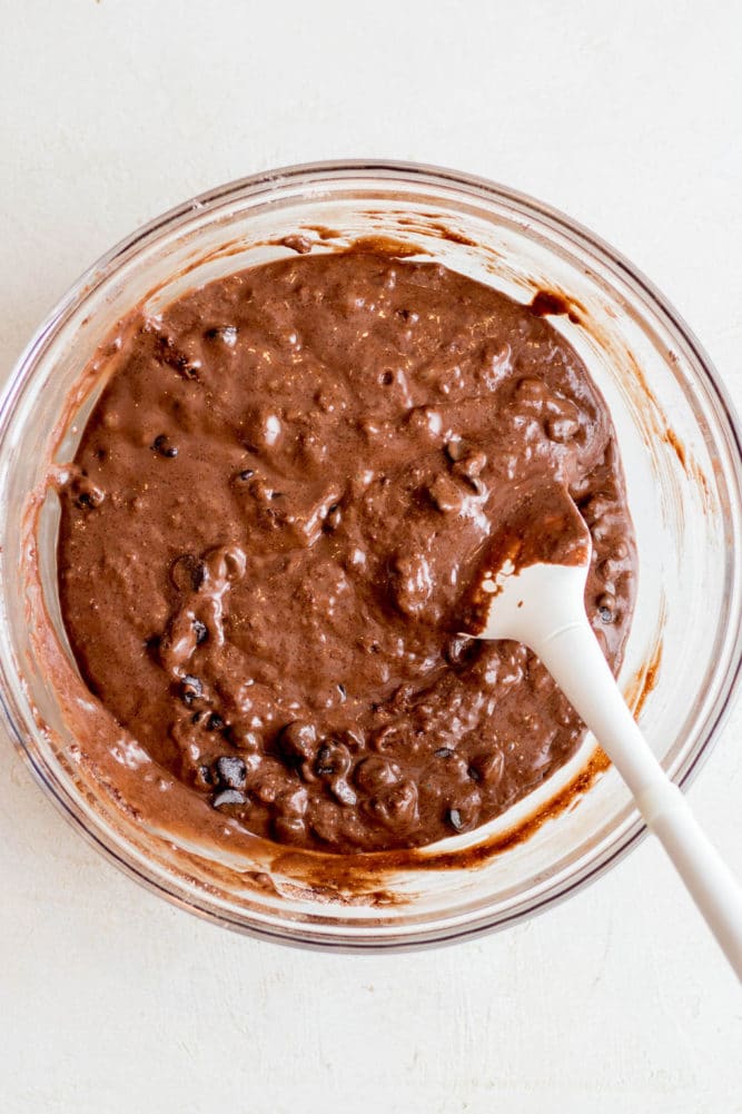 white spatula folding chocolate chips into chocolate muffin batter.