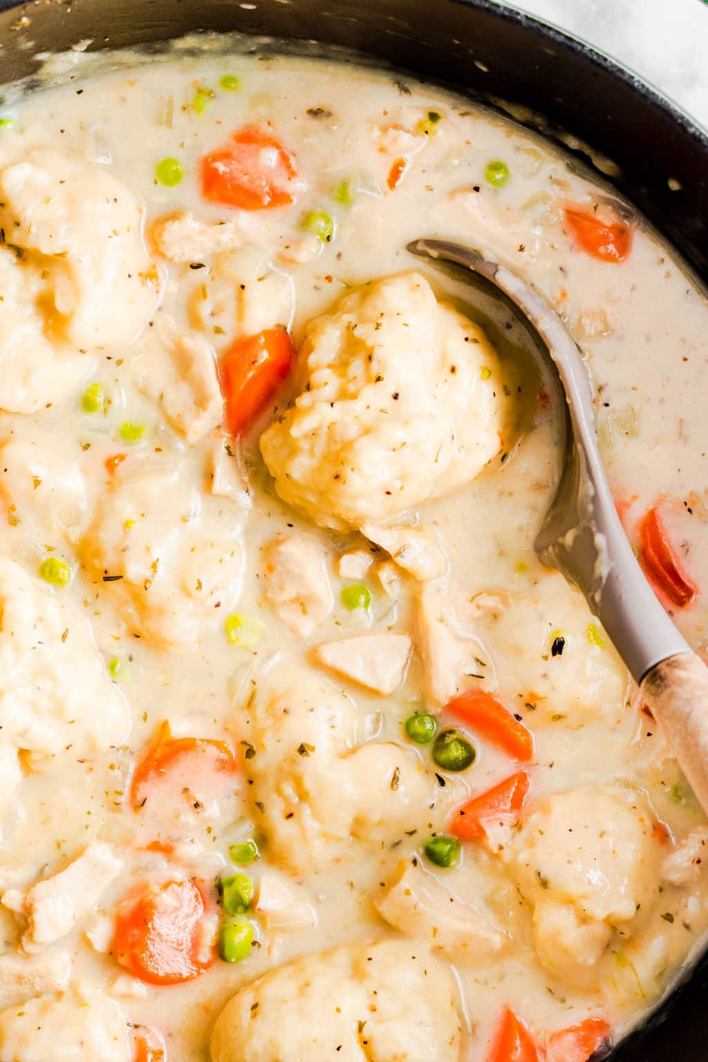 large spoon scooping a dumpling from a large black pot filled with vegan chicken soup and dumplings.