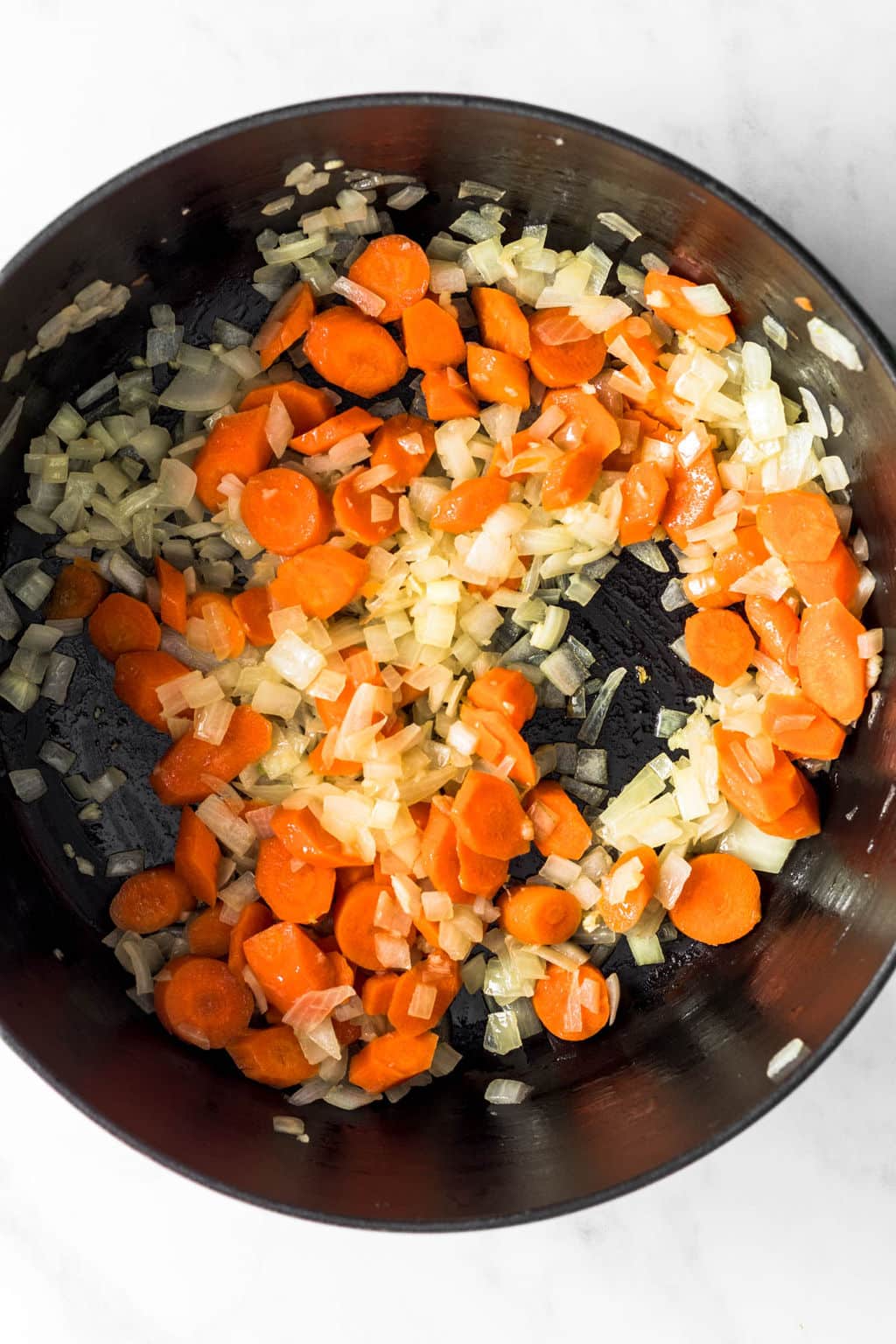 sautéing carrots and onions together in a large black pot.