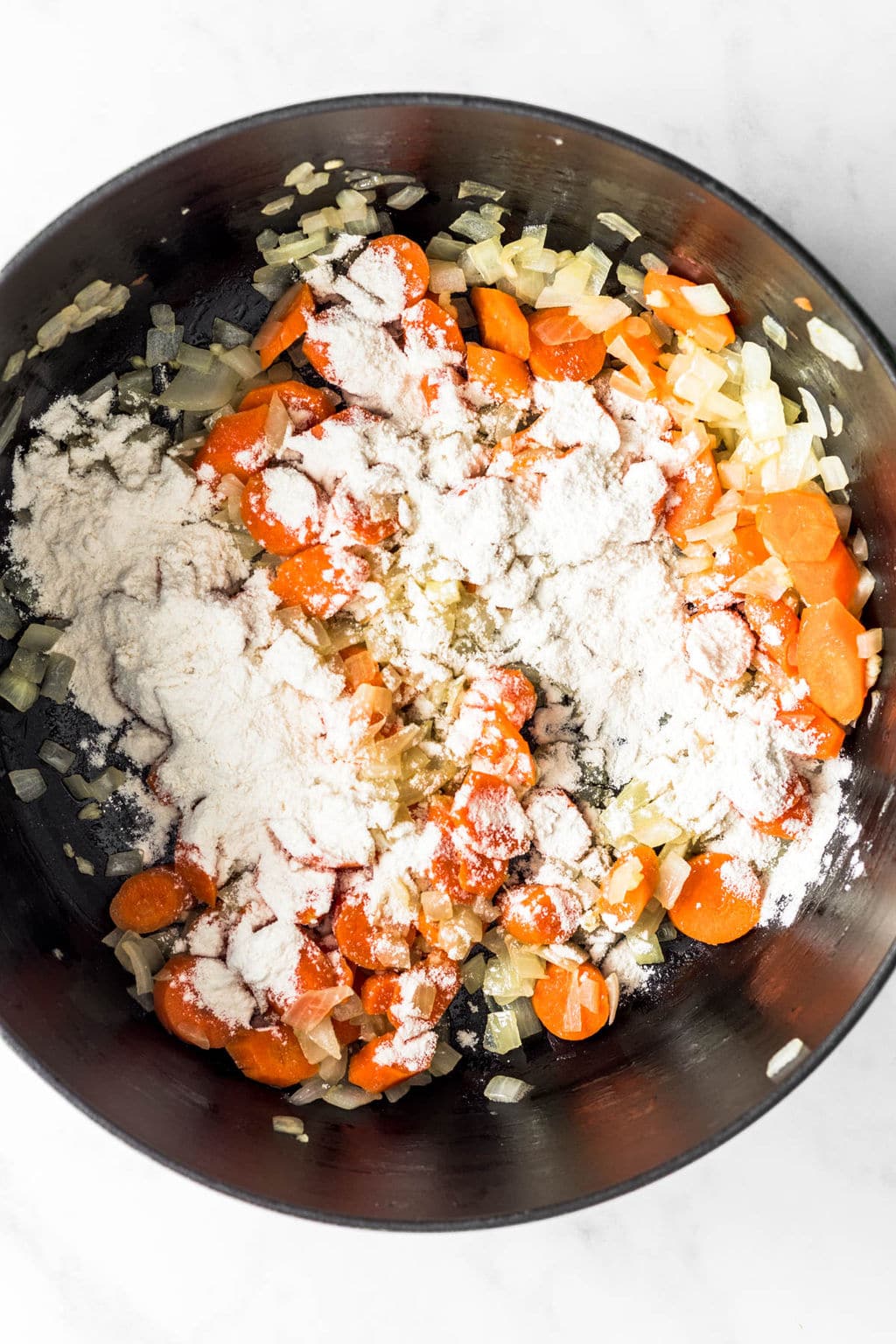 sauteed carrots and onions in a large black pot covered in flour.