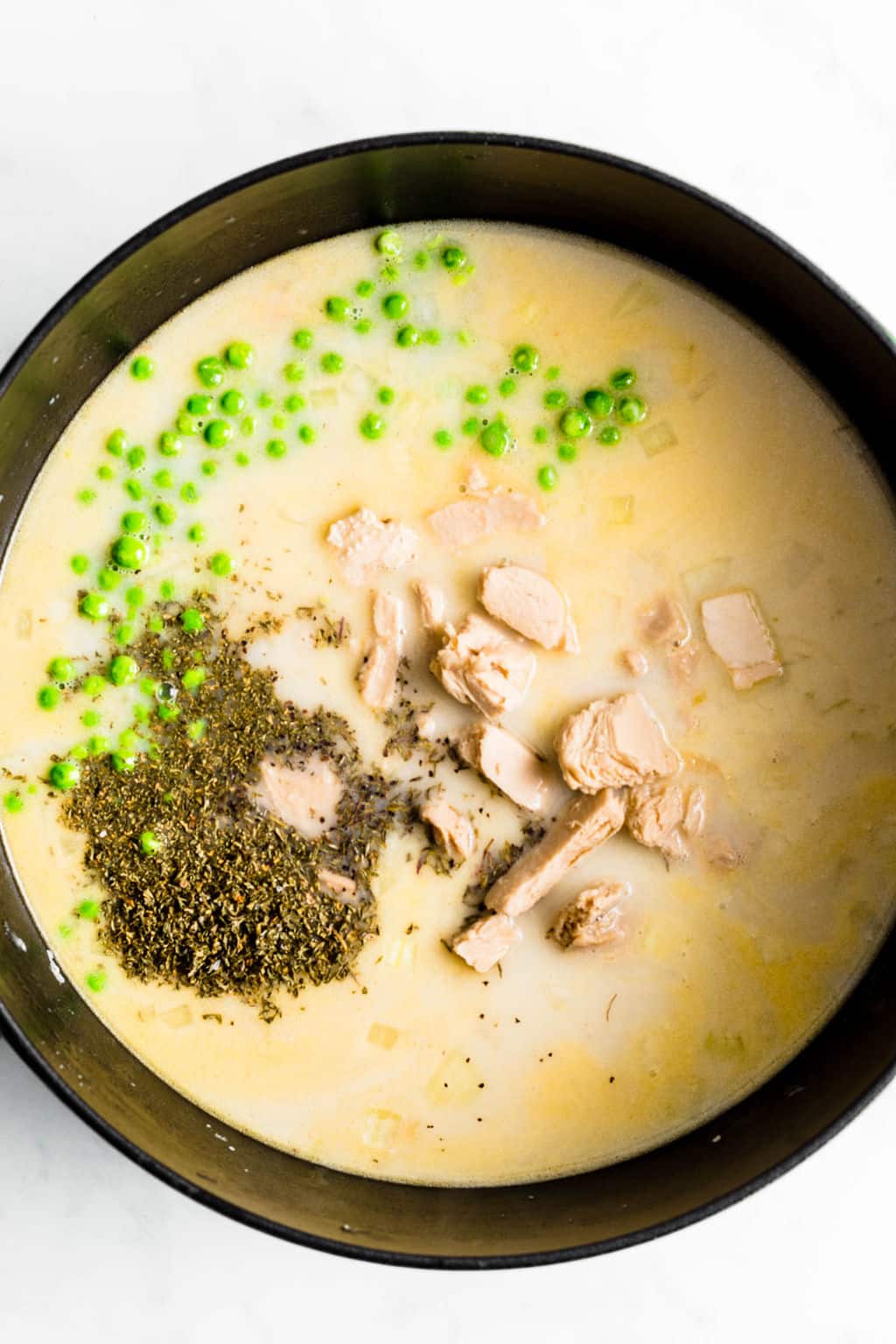 large black pot filled with a creamy liquid, vegan chicken, dried herbs, and green peas.