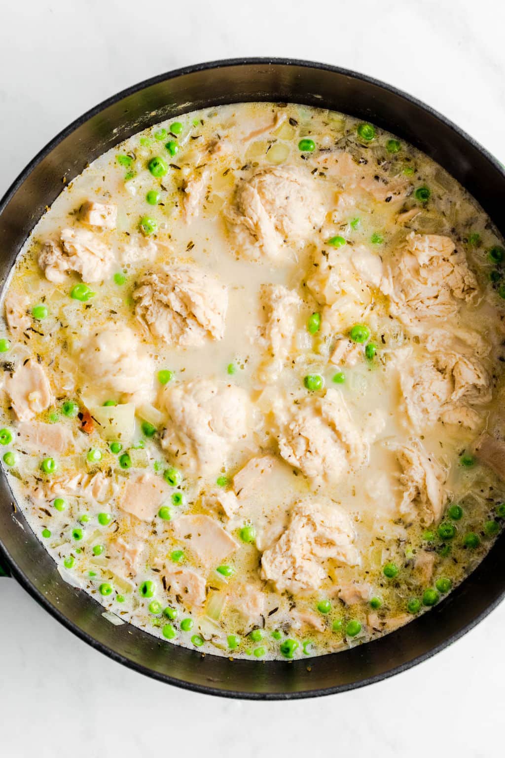 raw dumplings cooking in a large black pot filled with a creamy chicken soup.